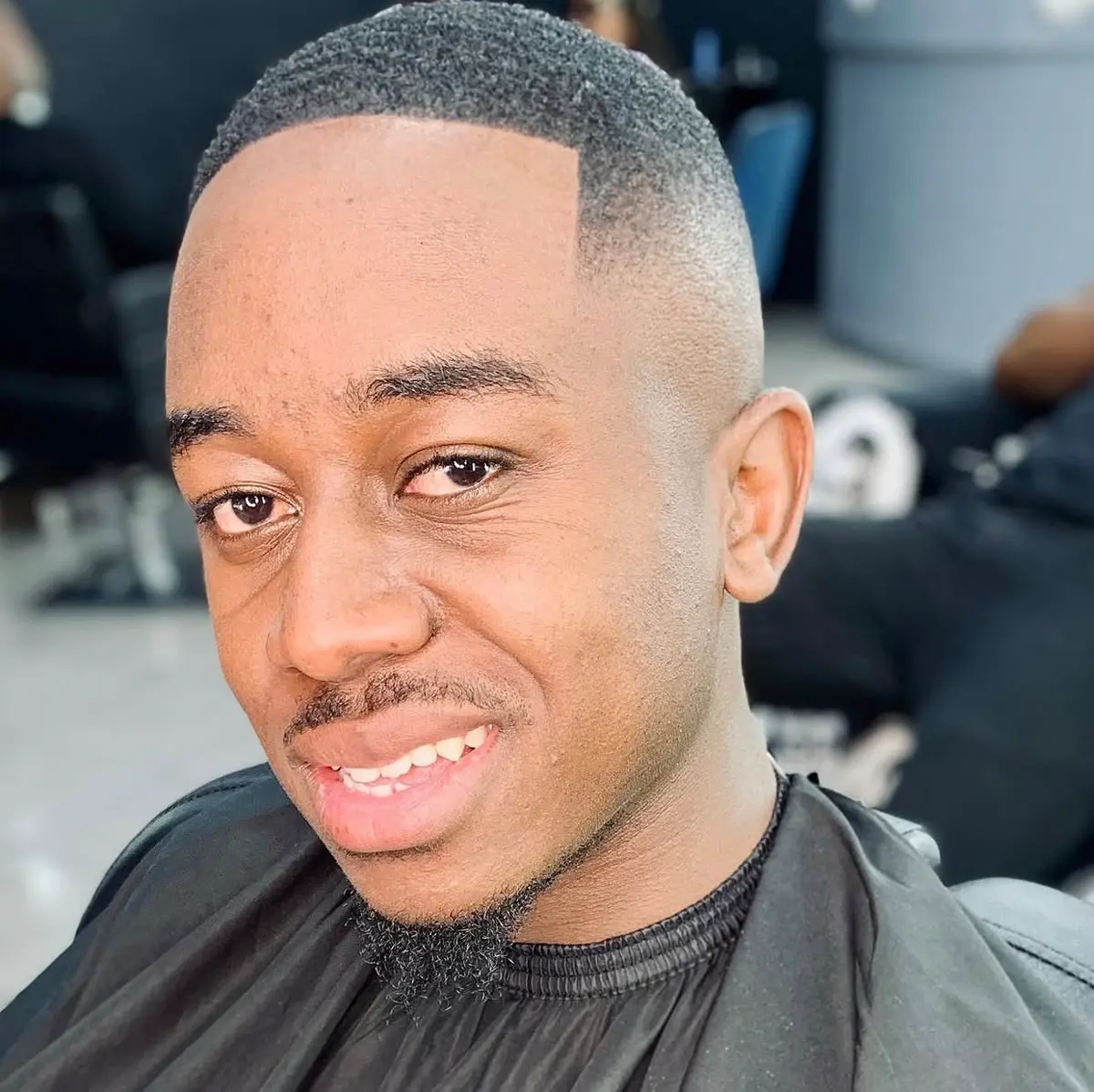 Smiling man with a fresh short haircut wearing a black barber cape